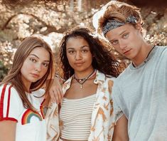 three young people standing next to each other with trees in the back ground behind them