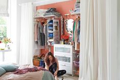 a woman kneeling on the floor in front of a closet filled with clothes and other items