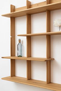 a wooden shelf with two bottles and a vase sitting on top of it, in front of a white wall