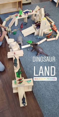 a child playing with dinosaurs on the floor in front of a wooden toy land set