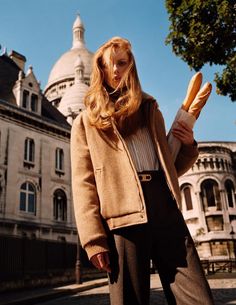 a woman standing in front of a building with a loaf of bread on her hand