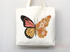 a white tote bag with an orange butterfly and flowers on the front, hanging from a hook