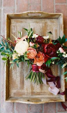 a bridal bouquet with red and white flowers on a wooden frame in front of a brick wall