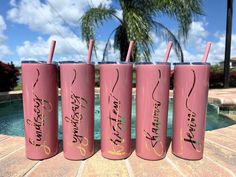 four pink tumblers with writing on them sitting next to a pool and palm tree