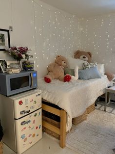 there is a small bed with teddy bears on it and a refrigerator in the corner