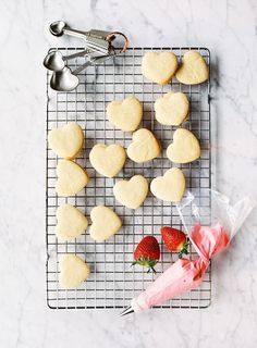 heart shaped sugar cookies on a cooling rack with strawberries and spoons next to them