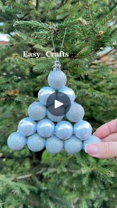 a hand holding a christmas ornament in front of a tree with the words easy crafts on it