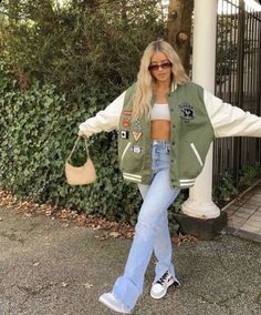 a woman standing in front of a fence with her arms spread out, wearing jeans and a jacket