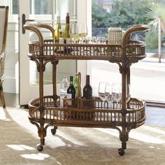 a wicker bar cart with wine bottles and glasses on it in front of a window