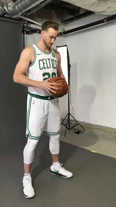 a man holding a basketball while standing in front of a white wall with lights on it