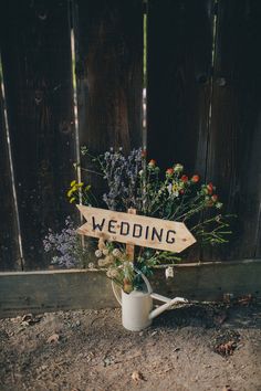 a bouquet of flowers in a watering can with a wooden sign that says'wedding '