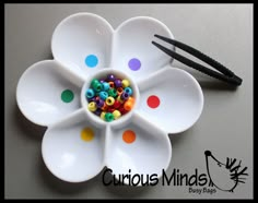 a white flower shaped bowl with colorful beads in it