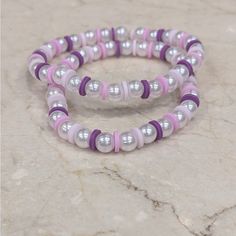 two bracelets with white and pink beads on a marble surface in front of a stone wall