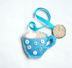 a felt tea cup ornament with buttons and a blue ribbon