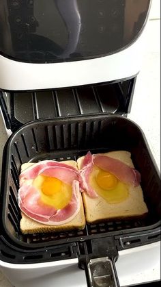 two pieces of toast with eggs on them sitting in an air fryer oven, ready to be cooked