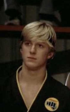 a young man with blonde hair wearing a black shirt and gold medal around his neck