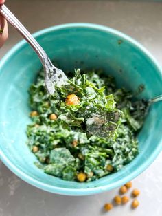 a person holding a spoon in a bowl filled with greens and chickpeas, ready to eat