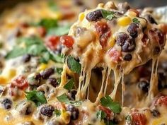 a spoon full of black beans and corn casserole being lifted from a skillet