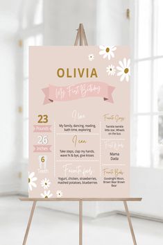 a pink and gold baby's first birthday calendar on a easel in front of a window