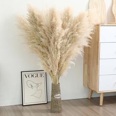 a vase filled with dry grass sitting on top of a wooden floor next to a white dresser