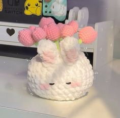 a crocheted white and pink stuffed animal with flowers in it's mouth