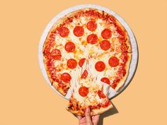 a person holding up a large pizza with pepperoni on it in front of an orange background