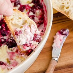 a person dipping something into a bowl with cranberries and cream cheese on top