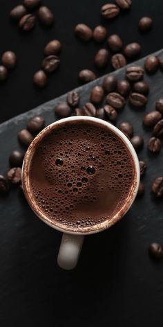 a cup of coffee sitting on top of a table next to some roasted coffee beans