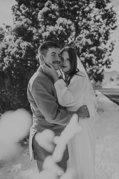 a bride and groom embracing each other in front of a tree on their wedding day