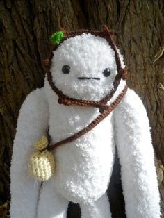 a white stuffed animal with a green leaf on it's head and neck, standing next to a tree