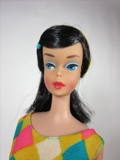 a doll with black hair and blue eyes wearing a multicolored dress on a white background