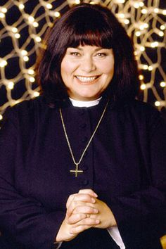 a woman wearing a priest's outfit standing in front of a wall with lights