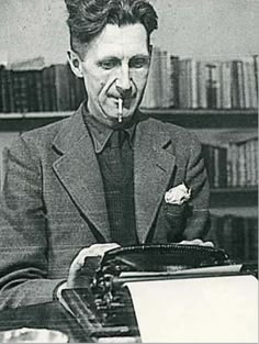 an old man sitting at a desk with a typewriter in front of his face