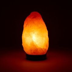 an orange himalayan stone lamp on a black base with red light in the dark background