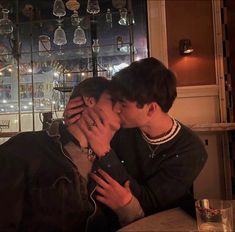 two young men sitting at a table kissing each other