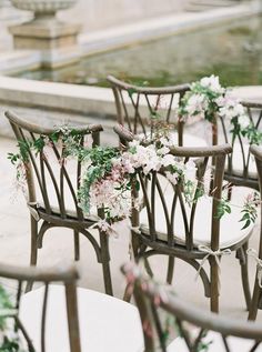 the chairs are decorated with flowers and greenery for an outdoor wedding ceremony in front of a fountain