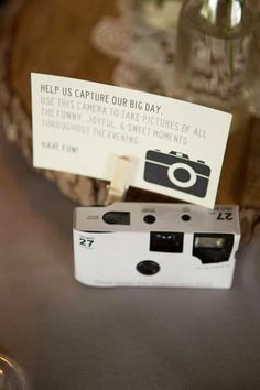 a white camera sitting on top of a table next to a glass vase filled with flowers