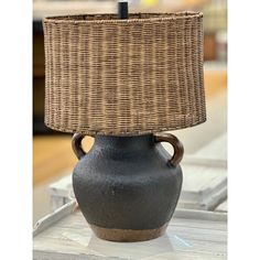 a black vase with a brown base and a light shade on the top is sitting on a table