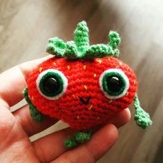 a hand holding a small knitted strawberry