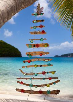 a wooden christmas tree hanging from the side of a palm tree on top of a beach