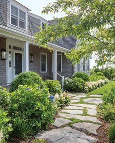 a stone path leads to the front door of a gray house with white trim and shingled windows