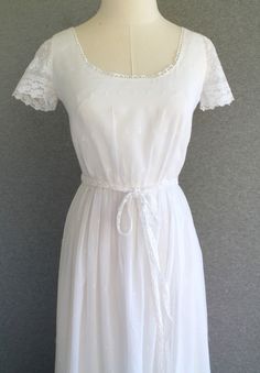 "This is a very sweet cotton batiste dress that is fully lined and features a lace hemline and sleeve.   The dress is in beautiful condition but does have a hole in the lining and the original lace sash has some breaks in the lace.  Please see pictures.  It is not attached and can easily be replaced.  Perfect for a country wedding. Shown on a size 4 dress form. Estimated size 2 to snug 4 32\"-34\"  bust 25\" waist full hip 56\" shoulder to hem  Purveyor's Note: We have searched far and wide, wre Fitted Swiss Dot Dress For Garden Party, White Swiss Dot Cotton Dress, Fitted Swiss Dot Dress For Daywear, White Cotton Vintage Wedding Dress, Formal Fitted Broderie Anglaise Dress, White Broderie Anglaise Regency Dress, White Embroidered Cottagecore Dress, Cottagecore V-neck Dress With Lace Trim, White Lace Cottagecore Vintage Dress