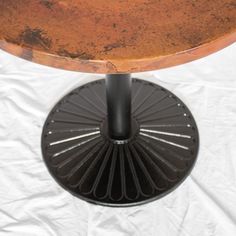 the top of a round table with a metal base and brown wooden top, on a white sheeted surface