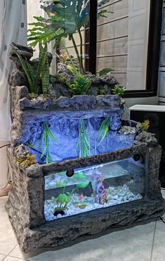 an aquarium with plants and rocks in the middle is displayed on a tile floor next to a window