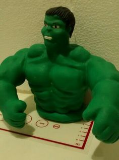 a green toy sitting on top of a table next to a measuring scale with the hulk