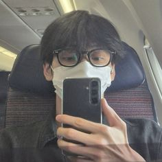 a man wearing a face mask while looking at his cell phone in the air on an airplane