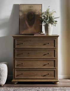 a wooden dresser sitting in front of a painting on the wall next to a plant