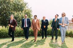 a group of men in suits and ties walking on the grass near some bushes with trees