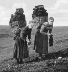 two women with baskets on their heads are standing in the grass, and one is holding something