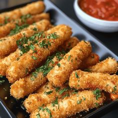 fried chicken sticks with parsley on top in a black tray next to a bowl of tomato sauce